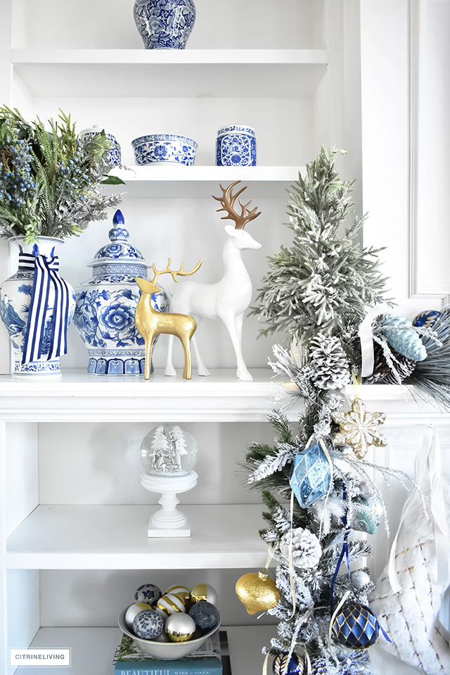 bookshelves-with-blue-and-white-christmas-decor-gold-accents-greenery-reindeer-flovked-garland